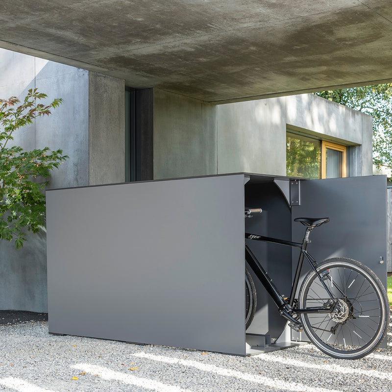 Geöffnete BikeBox smart Solo Design Fahrradgarage in Anthrazit mit einem Fahrrad vor einem modernen Wohnhaus.