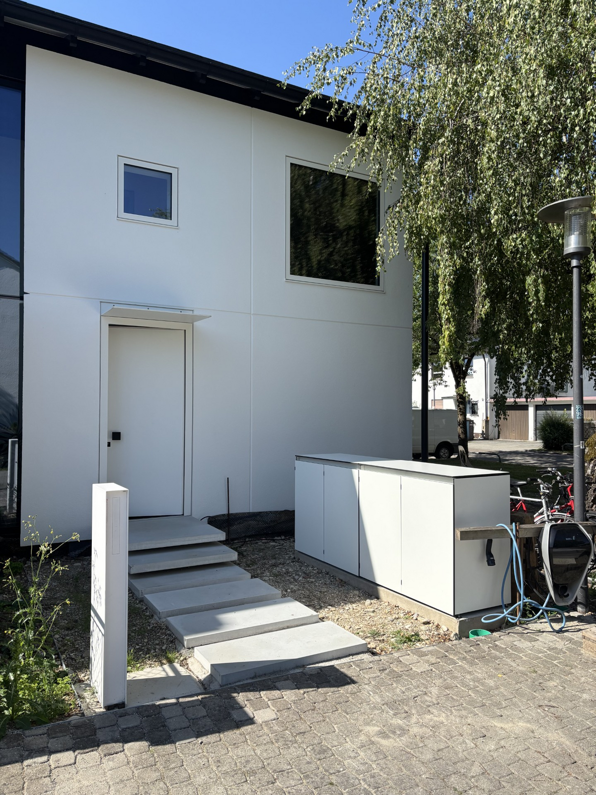 Moderner weißer Design Gartenschrank aus HPL neben einem modernen Wohnhaus im Außenbereich