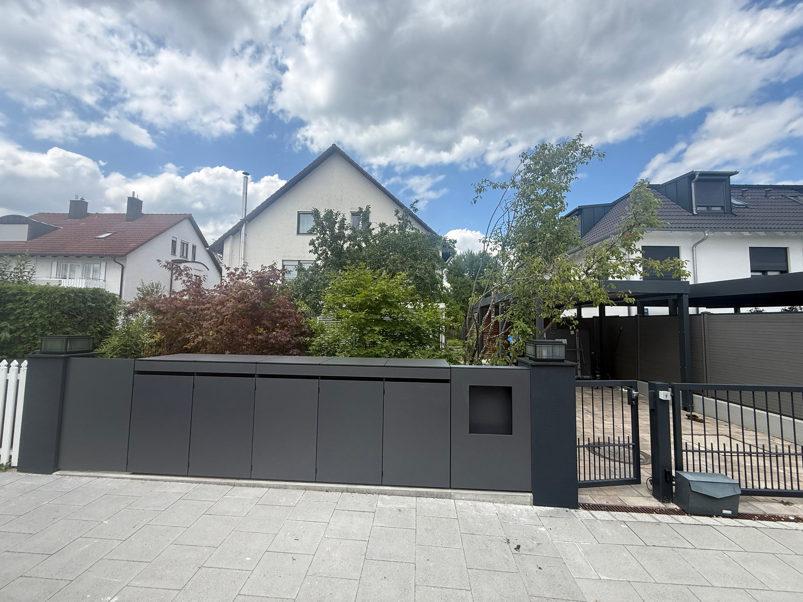 Moderne anthrazitfarbene Mülltonnenbox aus HPL mit integriertem Gartenzaun im Vorgarten